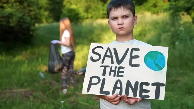boy child holds save planet poster looking to camera. volunteer activist children picking up plastic garbage collecting plastic bottles into trash bag. activists kids tidying up rubbish outdoors