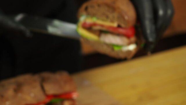 the chef cuts a sandwich with cheese, herbs and meat and shows the cut to the camera.4K video. the image is initially out of focus to give an effect