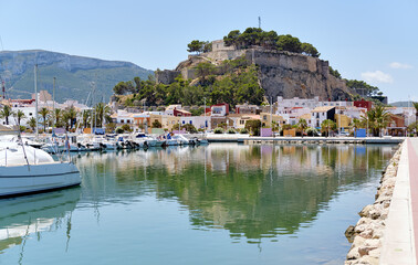 Fototapeta na wymiar Waterside view to moored yachts at harbour, old famous Denia Castle located on rocky hilltop mountain. Heart of ancient city, landmark and tourism concept. Alicante province, Costa Blanca, Spain