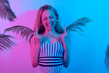 A girl in neon shows a fak on the background of tropical leaves.