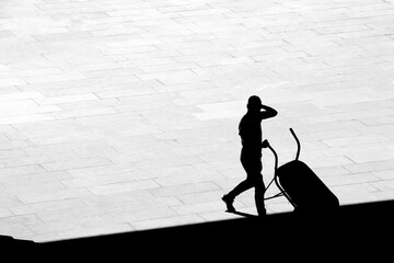 Silhouette of a man emptying a wheelbarrow on pavement in high contrast black and white