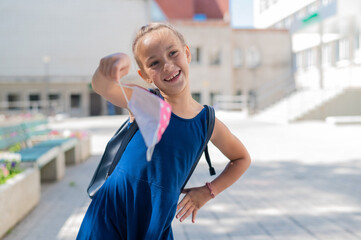 Happy schoolgirl takes off the mask. Joyful smiling girl with a backpack removes the mask and goes...