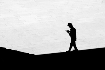 Silhouette of a man  smoking a cigarette while walking from the shade on the town square
