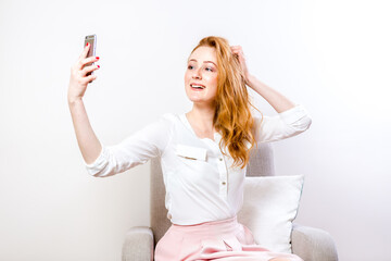 A young red-haired woman uses a mobile phone for video communication. Student on online confession on a white background. Female chatting on social network live in studio