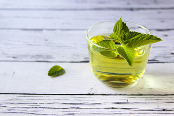 Fresh mint tea concept on a wooden background. Mint tea in a transparent cup and one mint leaf on the table