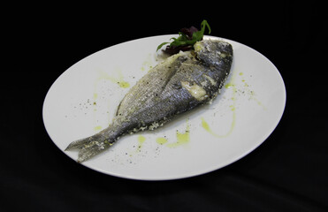 A piece of fried fish with basil on the white plate