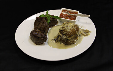 Fried meat, sauce, baked potato with mushrooms, and basil leaf on the plate. Close-up
