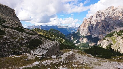 Italy dolomite landscape in summer. Valley, hiking trail and a sprawled wooden barn. Mountain range from all sides