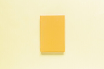 Closed yellow notebook on yellow background. Top view, mockup