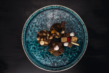muffins stuffed with delicacy and decorated with chocolates and different sweets on blue plate with black background