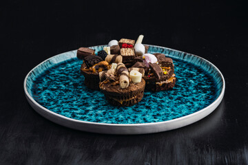 muffins stuffed with delicacy and decorated with chocolates and different sweets on blue plate with black background
