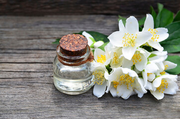 Jasmine essential oil in a glass bottle and fresh jasmin flowers on old wooden background.Aromatherapy,spa or wellness concept.Selective focus.