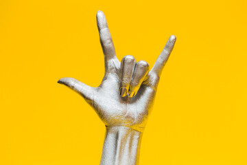 Elegant female hand with a silver paint on it shows gesture rock isolated on a yellow background. Free space for text