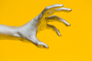 Elegant female hand with a silver paint on it shows gesture wild isolated on a yellow background. Free space for text