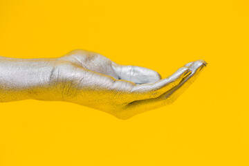 Elegant female hand with a silver paint on it shows open palm, isolated on a yellow background. Free space for text