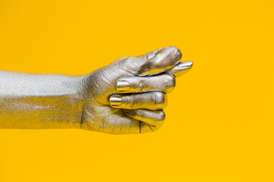 Elegant female hand with a silver paint on it shows fig sign isolated on a yellow background. Free space for text