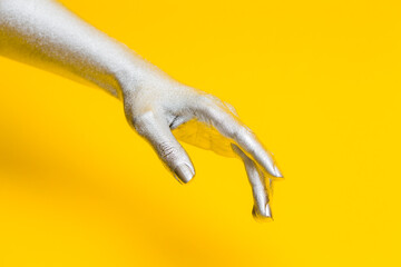 Elegant female hand with a silver paint on it isolated on a yellow background. Free space for text