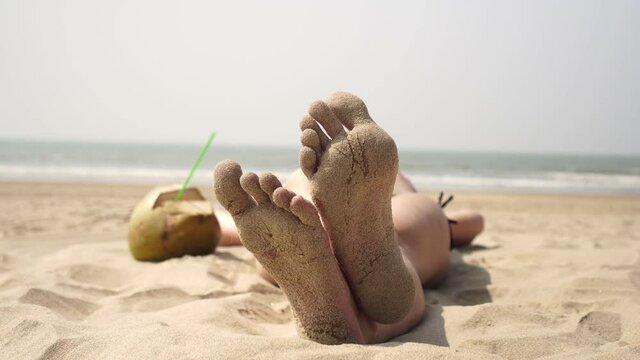 A woman is relaxing and sunbathing on a tropical sea beach. Feet in sand closeup