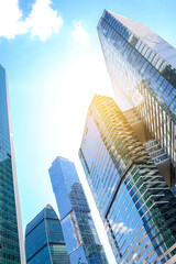 Low angle view of large skyscrapers covered with glass. Blue sky with some white clouds in the background. Modern office buildings theme.