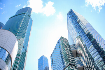 Obraz premium Low angle view of large skyscrapers covered with glass. Blue sky with some white clouds in the background. Modern office buildings theme.