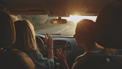 Rear view of cheerful young girlfriends singing their favourite song and dancing while driving at sunset. Two beautiful women travelling and having good time together . Concept of friendship - Powered by Adobe