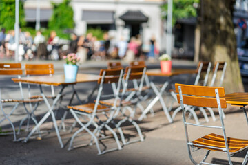 Wooden chairs in outdoor restaurant with fresh plant and flowers on the table in public area with a lot of people in the background on a sunny day