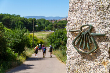 Pilgrims on the route of the Camino de Santiago (Way of Saint James) passing next to the scallop shell that marks the way
