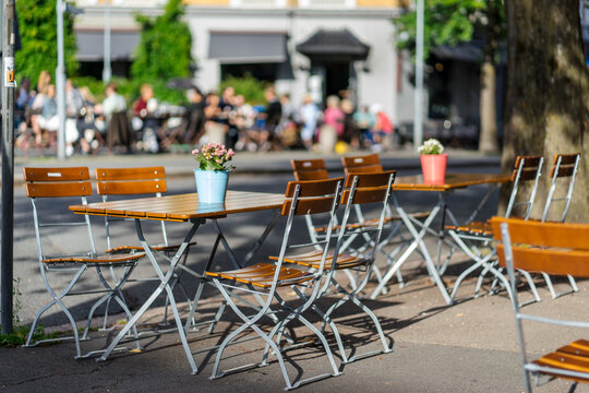 Wooden chairs in outdoor restaurant with fresh plant and flowers on the table in public area with a lot of people in the background on a sunny day