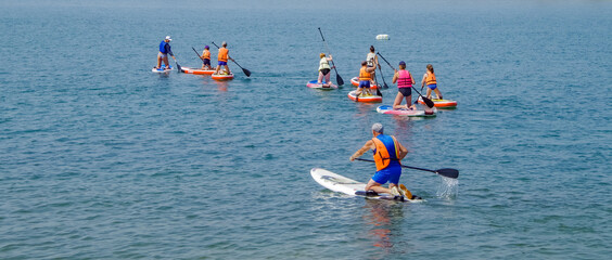 group of surfers on boards for sap surfing with oars have fun together, concept of active lifestyle