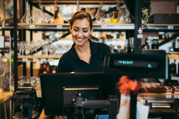 Beautiful and positive female cashier working on cash register in a modern supermarket or grocery store. - obrazy, fototapety, plakaty