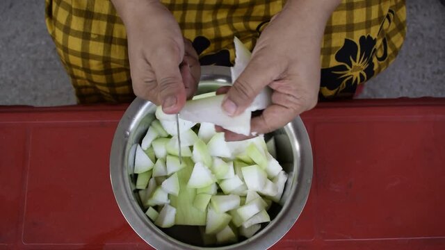 Gurgaon, India 2020: Cutting of Vegetable by a small knife into small pieces. Indian house wife chopping bottle gourd into small pieces and putting them in the steel bowl