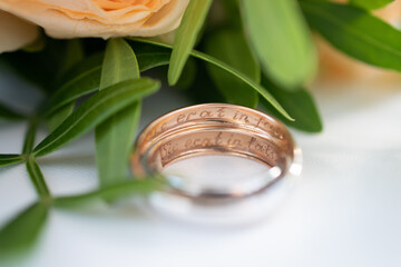 Two wedding rings in yellow and white gold, engraved with the Latin words "so fated" on the background of a wedding bouquet of roses. Wedding concept, romantic greeting card. Extra macro