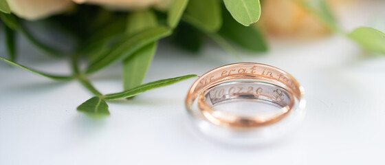 Two wedding rings in yellow and white gold, engraved with the Latin words "so fated" on the background of a wedding bouquet of roses. Wedding concept, romantic greeting card. Banner