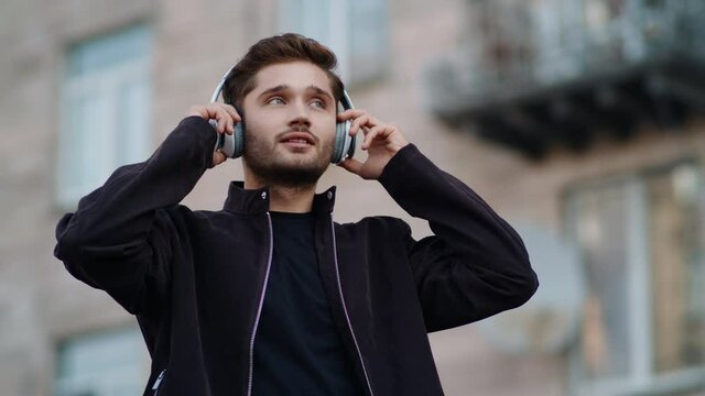 Happy guy listening music with headphones outdoors. Chherful man dancing outside