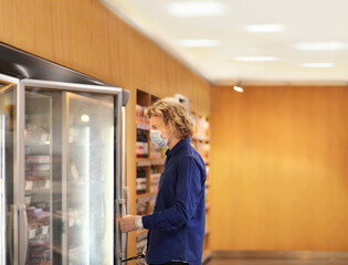 Fototapeta na wymiar supermarket shopping, face mask and gloves,Man choosing frozen food from a supermarket freezer 