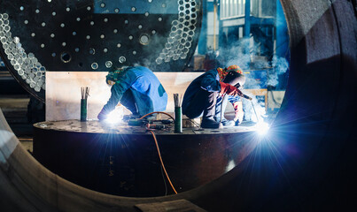 Two workers welding in a factory manufacturing boilers