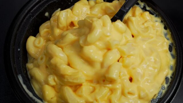 This POV closeup video shows a plastic spoon stirring and serving bowl of delicious macaroni and cheese.