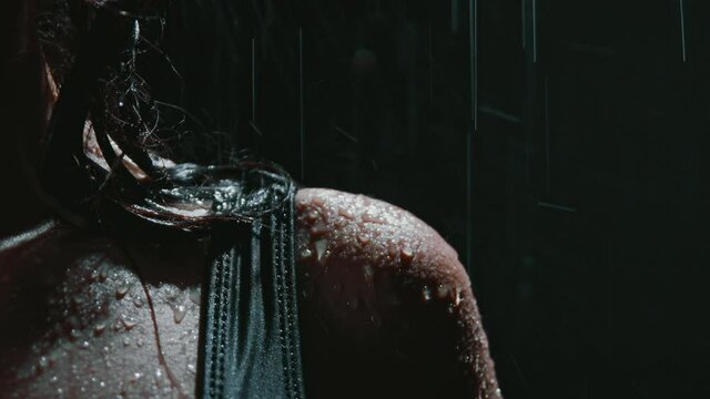 Drops of heavy rain hit the skin. Female shoulder is wet under the water falling down. Sad despair mood. A girl in a black swimsuit close-up. Concept of depression, fear, resentment.