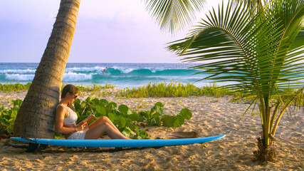 CLOSE UP: Woman relaxes on the beach near a popular surf spot and reads a book.