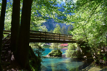A bridge over a magnificent crystal-clear blue lake in the mountains. Swiss Alps. Summer mountain landscape. Blue water, forest.