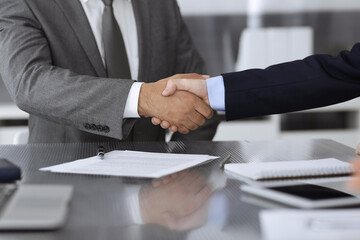 Unknown business people are shaking hands after contract signing in modern office, close-up. Handshake as successful negotiation ending