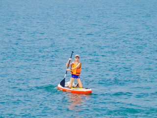 a young rider on a board for Sap surfing rakes a wave with a paddle, the concept of an active...
