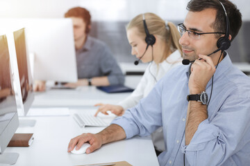 Fototapeta premium Call center. Group of casual dressed operators at work. Adult businessman in headset at customer service office. Telesales in business