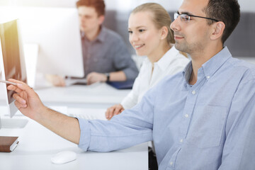 Fototapeta premium Business people working together in modern office. Happy smiling adult businessman using pc computer with colleagues. Teamwork and partnership concept