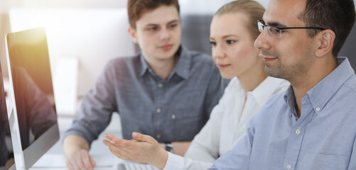 Fototapeta premium Business people working together in modern office. Happy smiling adult businessman using pc computer with colleagues. Teamwork and partnership concept