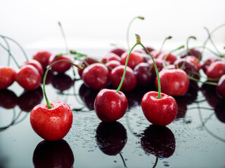 Red cherries in drops of water on a black background. Berries are reflected on a mirror background. Background with cherries.