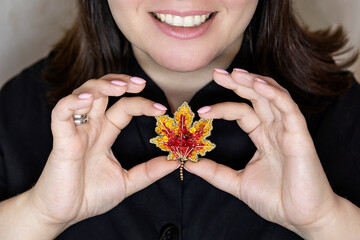 Handmade designer brooch in the shape of an autumn maple leaf made of beads in a female hand. Design solution, selective focus.