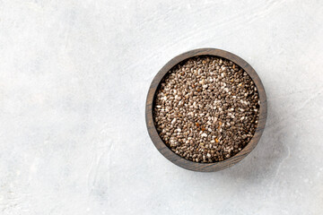 Chia seeds in a wooden bowl on a light gray background. Top view.
