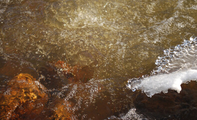 bubbles and foam on brown river water with ice and snow parts in sunny winter day.