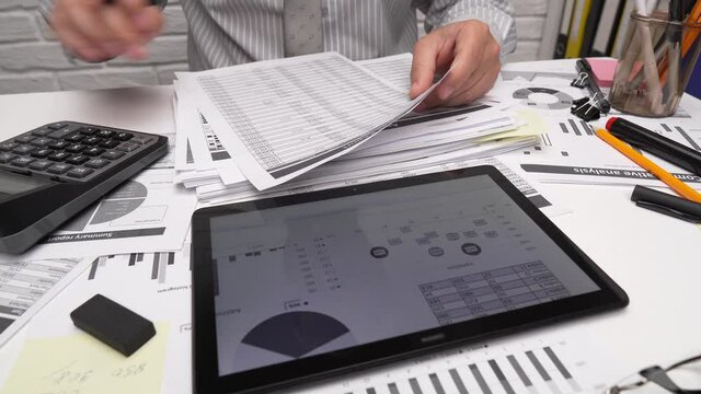 Business analysis and accounting concept - businessman working with document, spreadsheet, using calculator, tablet pc. Office desk closeup. 

